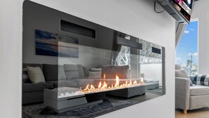 Ein modernes Wohnzimmer mit integriertem Kamin, grauen Sofas und einem großen Fenster mit Blick auf die Stadt.