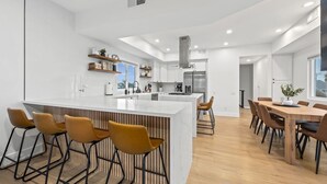 Eine moderne Küche mit Kochinsel, Barhocker und einem Essbereich mit Holztischen und -stühlen.