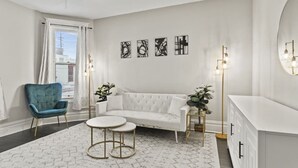 A modern living room with a white sofa, a blue armchair, two round tables, and a floor lamp. - Family Friendly Home for 8 (Fort Wayne)