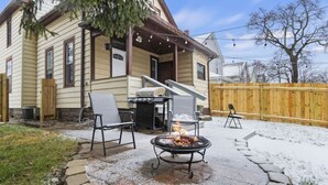 A house with a covered patio area featuring a fire pit, outdoor seating, and a wooden fence in the background. - Family Friendly Home for 8 (Fort Wayne)