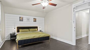A bedroom with a bed, a nightstand, a ceiling fan, and a door.