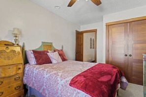 Une chambre à coucher comprenant un lit, une commode, une armoire et un ventilateur de plafond.