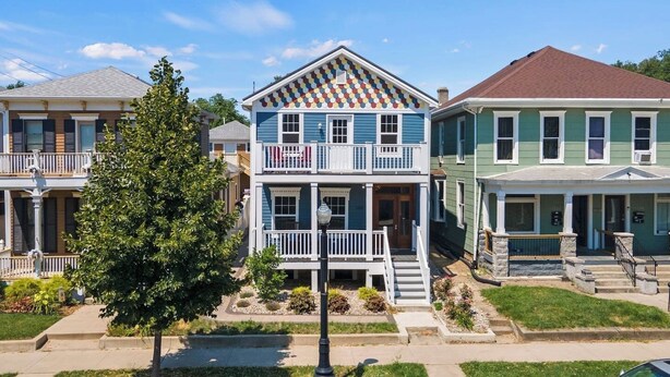A row of two-story houses with front porches and a tree in the foreground. - Apartment Near Parkview Field | Free Parking, Downtown Area (Fort Wayne)