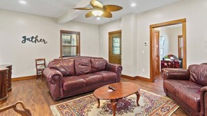 A living room with a leather sofa, a coffee table, a ceiling fan, and a rug. - Apartment Near Parkview Field | Free Parking, Downtown Area (Fort Wayne)