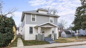 A two-story residential house with a front porch, a garage, and a well-maintained lawn. - Apartment with Private Fenced Yard | Pets Welcome (Fort Wayne)