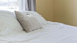 A neatly made bed with white bedding and a single gray pillow. - Apartment with Private Fenced Yard | Pets Welcome (Fort Wayne)