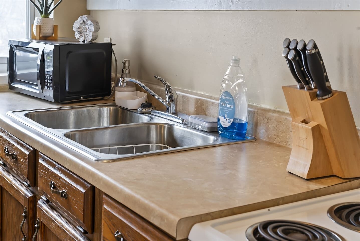 A kitchen with a double sink, a microwave, a dish soap bottle, and a knife block.