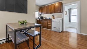 A modern kitchen with wooden cabinets, a white stove, and a dining table with benches. - Apartment with Private Fenced Yard | Pets Welcome (Fort Wayne)