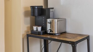 A kitchenette with a coffee maker, toaster, and two cups on a small table. - Apartment with Private Fenced Yard | Pets Welcome (Fort Wayne)