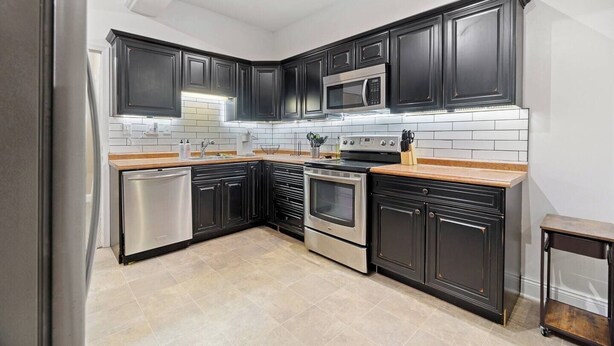 A modern kitchen with dark cabinetry, stainless steel appliances, and a tiled backsplash.
