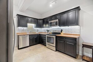 A modern kitchen with dark cabinetry, stainless steel appliances, and a tiled backsplash. - Historic Mansion Apartment | 2BR with Updated Amenities (Fort Wayne)