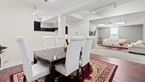 A dining area with a dark wooden table and white upholstered chairs, a red patterned rug, and a white sofa in the background.