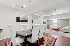 A dining area with a dark wooden table and white upholstered chairs, a red patterned rug, and a white sofa in the background.