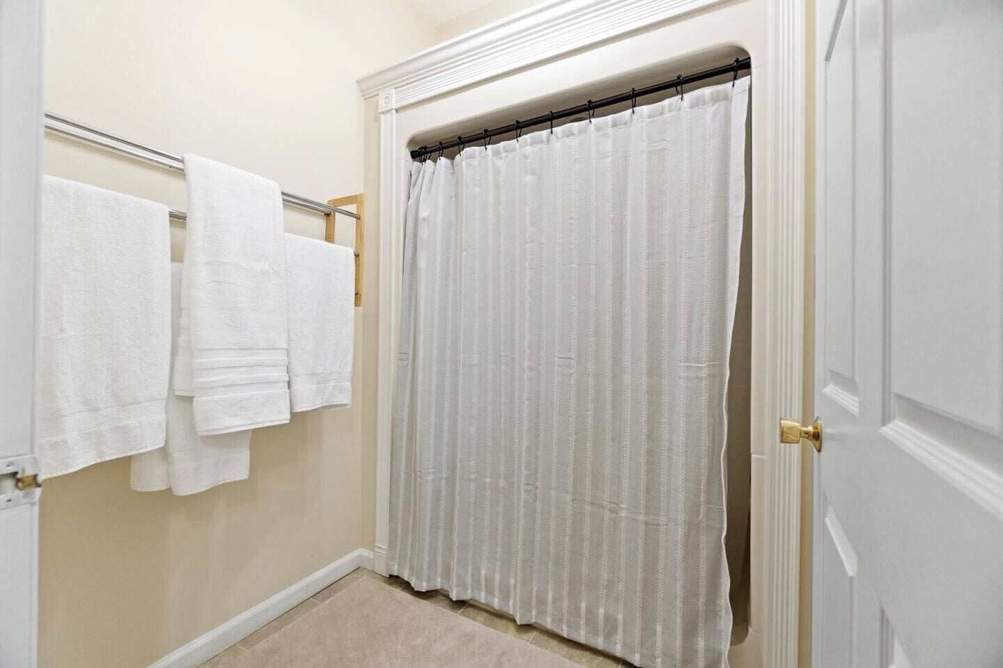A bathroom with a shower curtain, a towel rack with multiple towels, and a door.