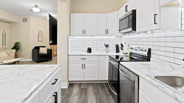A modern kitchen with white cabinetry, a black oven, and a stainless steel sink.