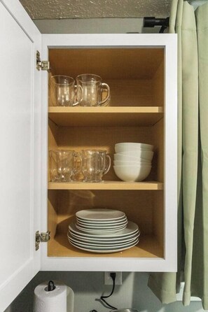 Un mueble con tazas de vidrio transparente, cuencos blancos y platos apilados.