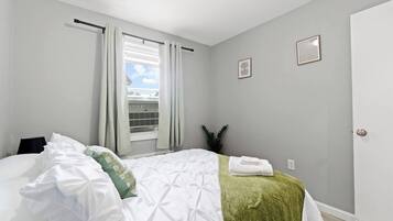 A bedroom with a bed, a window with curtains, a potted plant, and a door.