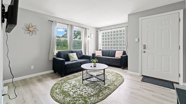A living room with two dark sofas, a round coffee table, and a large window with curtains.