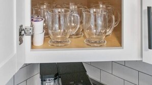 Et køkkenskab med to hylder, hver med flere glas og krus.