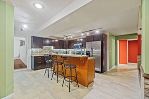 Una cocina con una isla central, armarios oscuros, electrodomésticos de acero inoxidable y un patrón de suelo en espiga.
