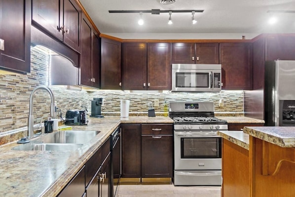 Una cocina moderna con armarios de madera oscura, electrodomésticos de acero inoxidable, encimera de granito y salpicadero con mosaicos.