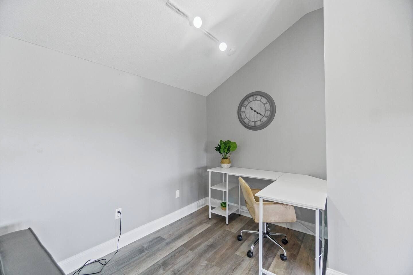 A room with a white desk, a chair, a clock on the wall, and a plant.