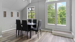 A dining area with a table and chairs, a window with a view of trees, and a ceiling light fixture.