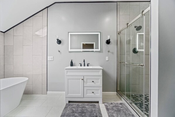 Un baño moderno con una bañera independiente, una ducha con cerramiento de vidrio y un tocador blanco con espejo.