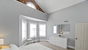 A bedroom with a large bed, a dresser, a mirror, a coat rack, and a skylight.