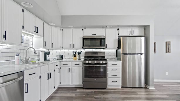 A modern kitchen with white cabinetry, stainless steel appliances, and a herringbone-patterned floor.