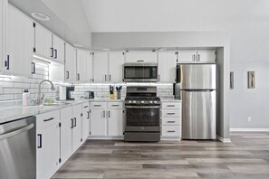 Una cocina moderna con armarios blancos, electrodomésticos de acero inoxidable y piso con patrón de espiga.
