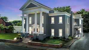 A large, two-story building with a central entrance flanked by columns, a brick facade, and a well-maintained lawn.