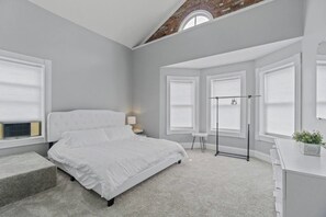 A bedroom with a bed, a desk, a chair, a lamp, and a window.