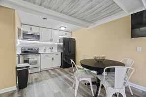 A compact kitchen with white cabinets, a microwave, a refrigerator, and a dining table with chairs.