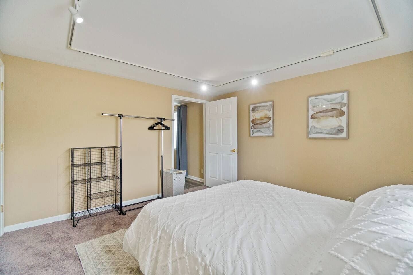 Een slaapkamer met een bed, een metalen droogrek, een deur en twee kunstwerken aan de muur.