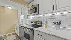 A modern kitchen with white cabinetry, a stainless steel oven, a microwave, and a marble countertop. - Downtown Apartment 3 in Historic Mansion | Free Parking (Fort Wayne)