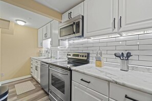 A modern kitchen with white cabinetry, a stainless steel oven, a microwave, and a marble countertop.
