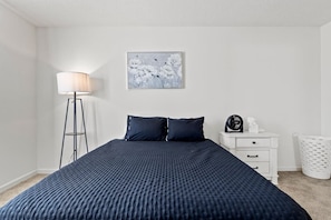 A bedroom with a bed, a bedside table, a lamp, a fan, and a trash bin. - Comfortable Home for 5 | Garage, Private Yard (Fort Wayne)