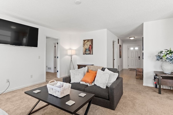 A modern living room with a gray sofa, a coffee table, and a TV mounted on the wall. - Comfortable Home for 5 | Garage, Private Yard (Fort Wayne)