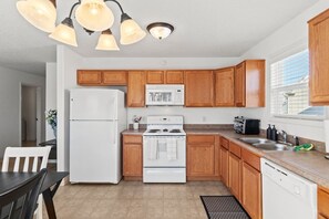 A kitchen with wooden cabinets, a white refrigerator, a stove, and a sink. - Comfortable Home for 5 | Garage, Private Yard (Fort Wayne)