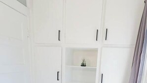 Une pièce avec une armoire blanche, une petite étagère et un plancher en bois gris.