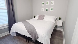 Un lit bien fait, avec une literie blanche et grise, un plaid gris et une petite plante sur une table de chevet.