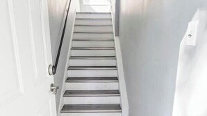 Un couloir étroit avec un escalier en bois menant à une porte portant des numéros.