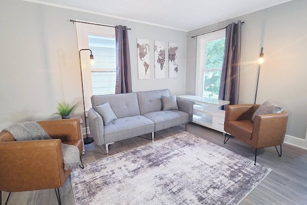 A modern living room with a grey sofa, two armchairs, a glass coffee table, and a patterned rug.