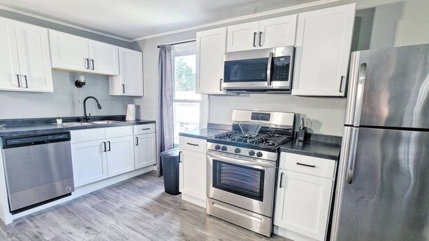 Une cuisine moderne dotée d’appareils électroménagers en acier inoxydable, de meubles blancs et d’un plancher en bois gris.