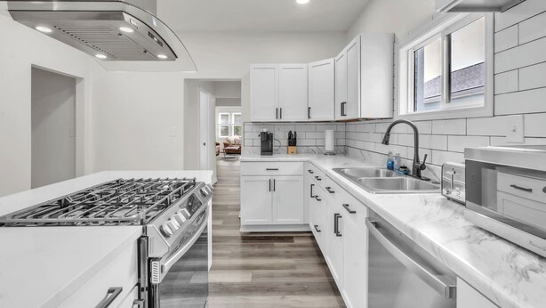 A modern kitchen with white cabinets, a stainless steel range, and a marble countertop.