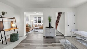 A spacious living area with a sofa set, a coffee table, and a cabinet. A staircase leads to another room.