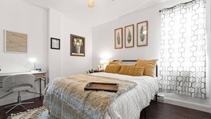 Une chambre à coucher comprenant un lit, un bureau, une chaise et une fenêtre agrémentée de rideaux à motifs.