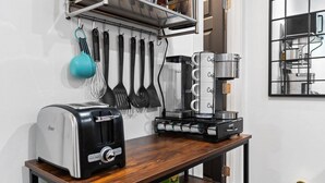 Une cuisine équipée d’un grille-pain, d’une machine à café et d’ustensiles de cuisine, le tout posé sur un plan de travail en bois.