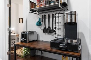 Une petite cuisine équipée d’une machine à café Keurig, d’un grille-pain et d’ustensiles de cuisine suspendus.